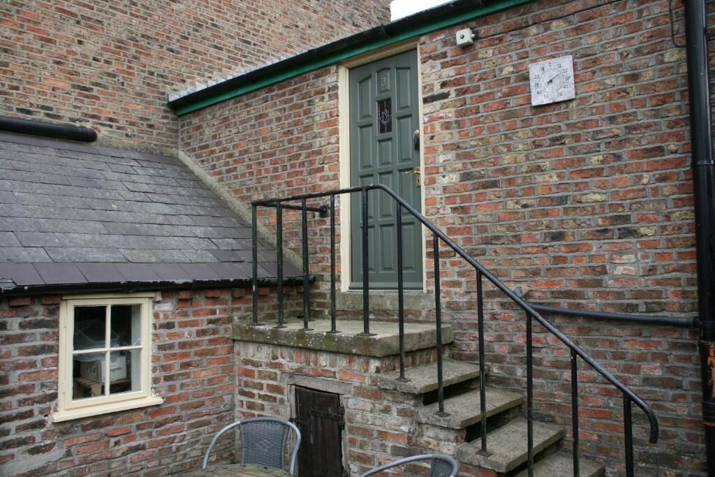 Un bâtiment en briques avec une porte verte, une fenêtre et un escalier en métal.