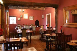 A dining area with wooden tables and chairs, framed pictures on the walls, and a chandelier. - Manor Guest House (York)