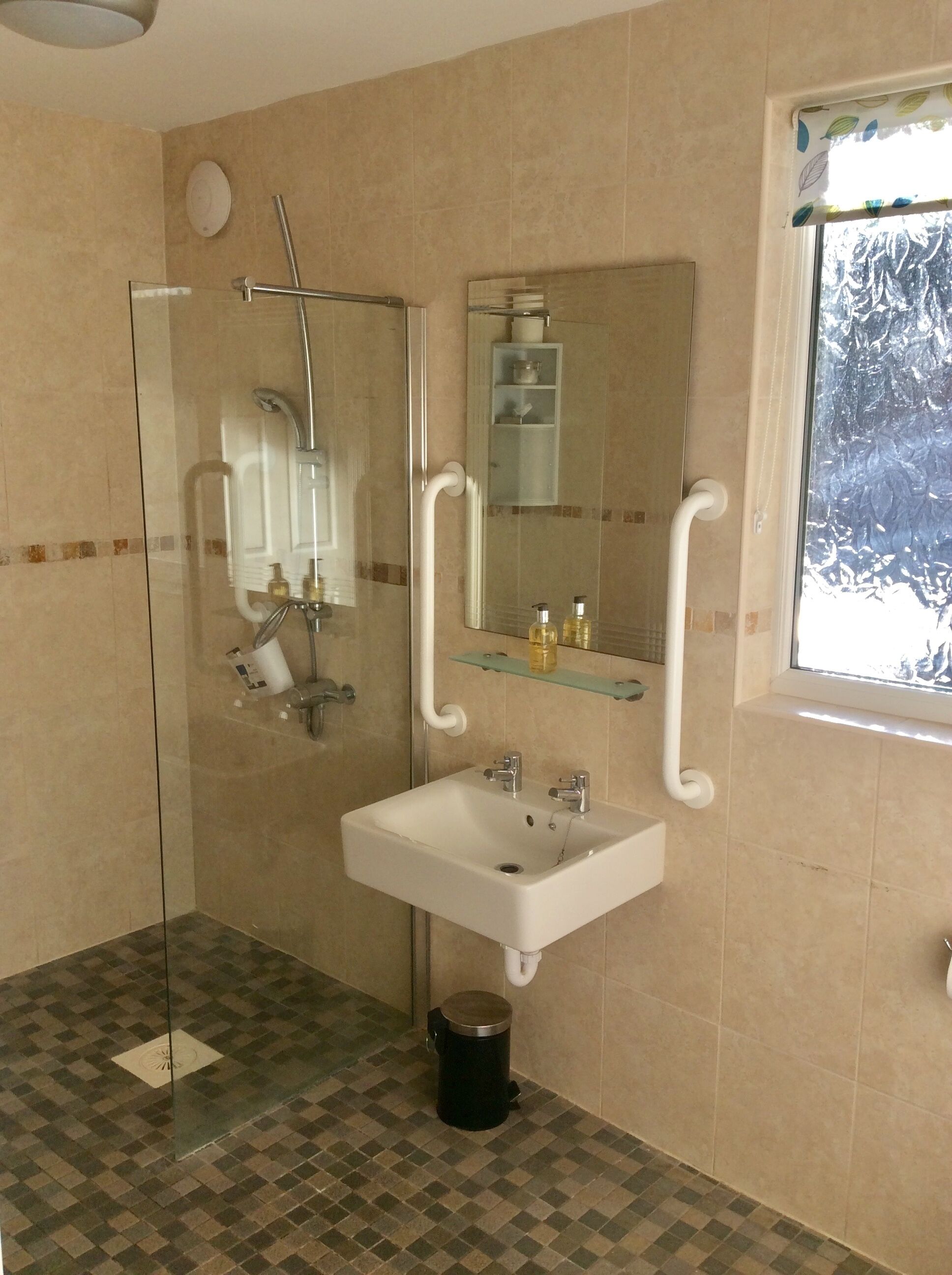 A bathroom with a glass-enclosed shower, a white sink, a mirror, and a window with a view of trees.