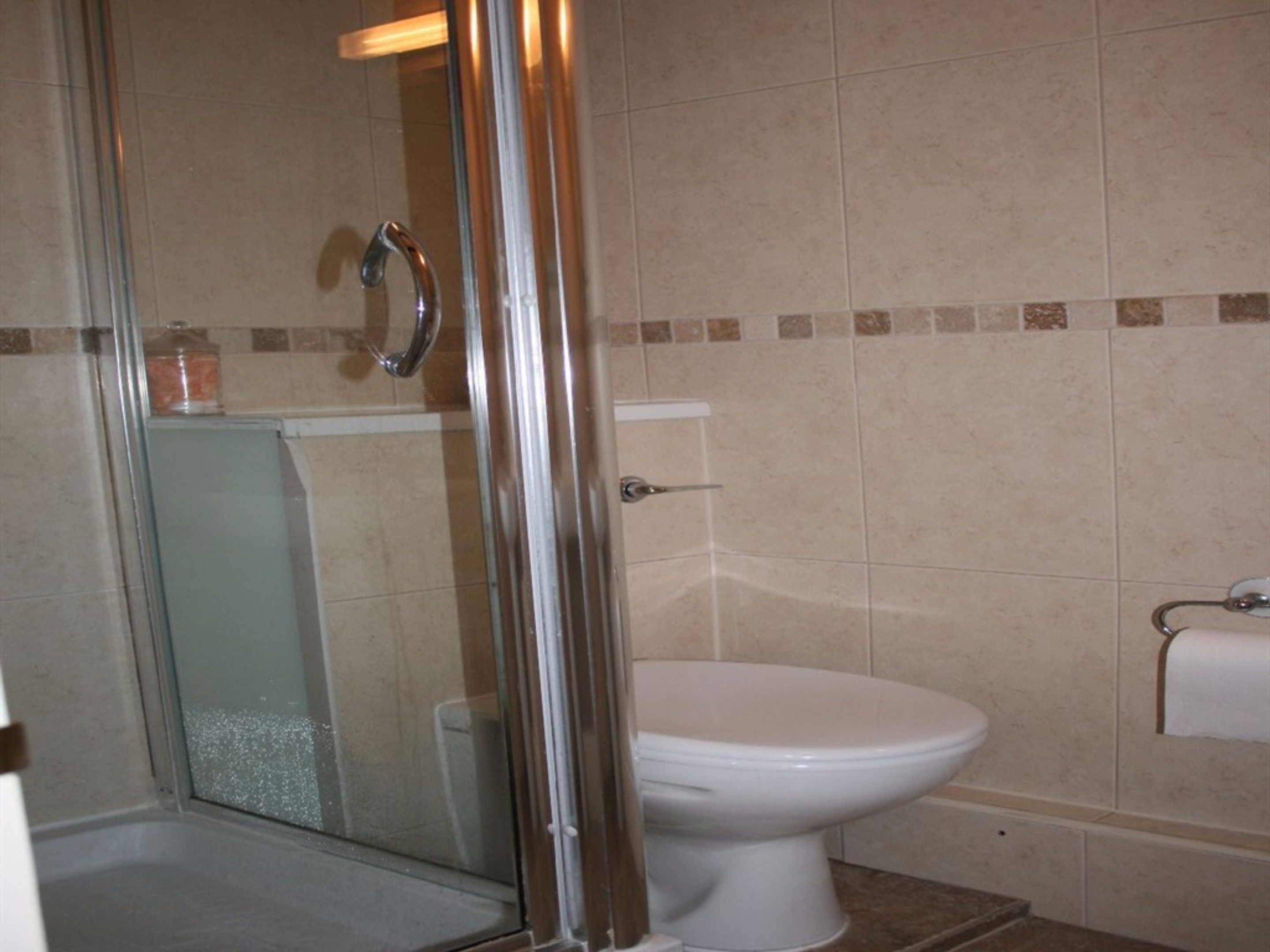 Une salle de bain avec une douche à parois de verre, des toilettes blanches et un porte-serviettes.