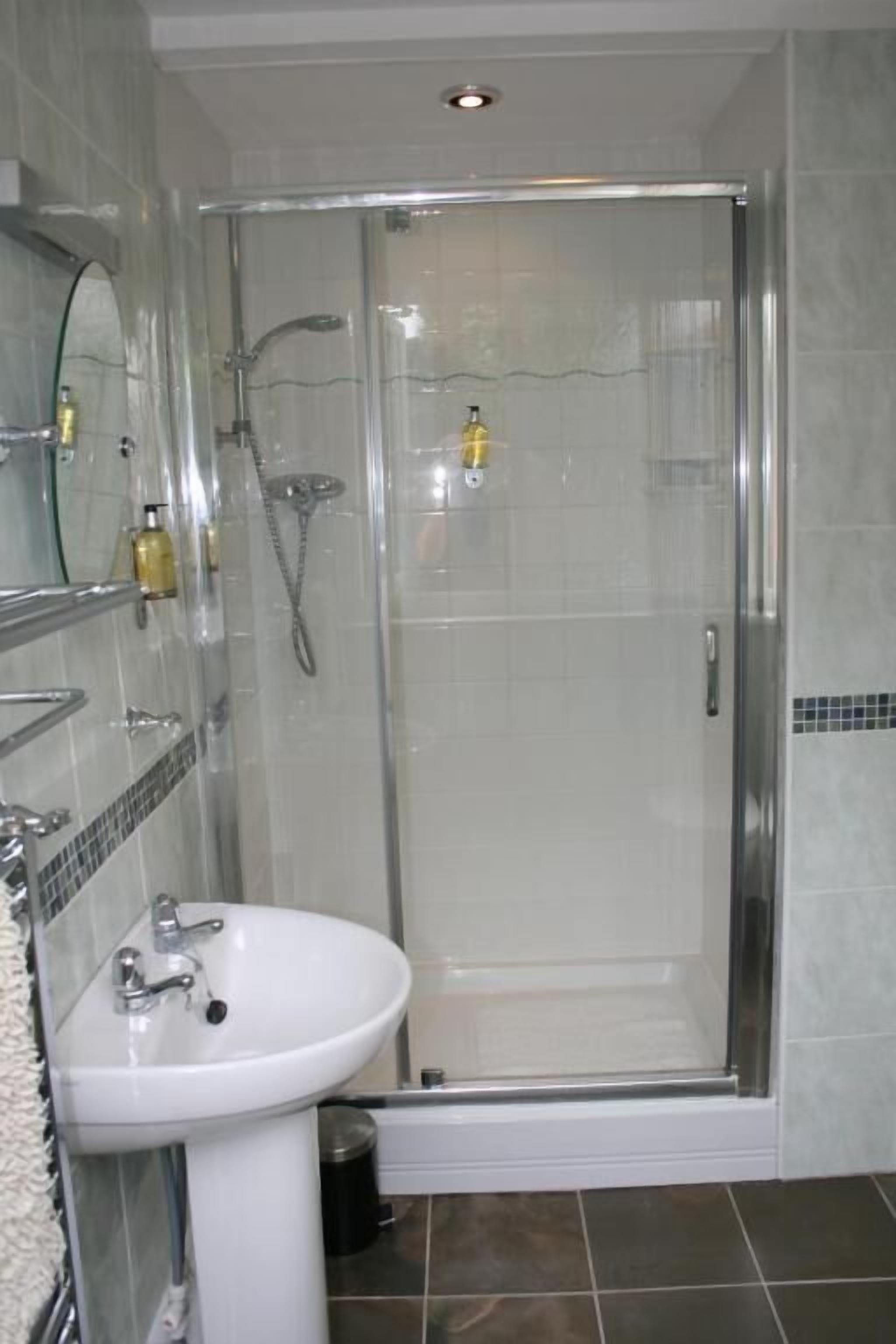 Une salle de bain dotée d’une douche à parois de verre, d’un lavabo sur pied blanc et d’un sol carrelé.