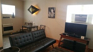 A living room with a black leather sofa, a glass-top dining table with chairs, a flat-screen TV on a wooden stand, and a radiator on the wall. - The Happy Hollow (Hot Springs)