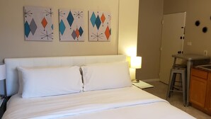 A hotel room with a bed, bedside table, lamp, and a kitchenette area. - The Happy Hollow (Hot Springs)