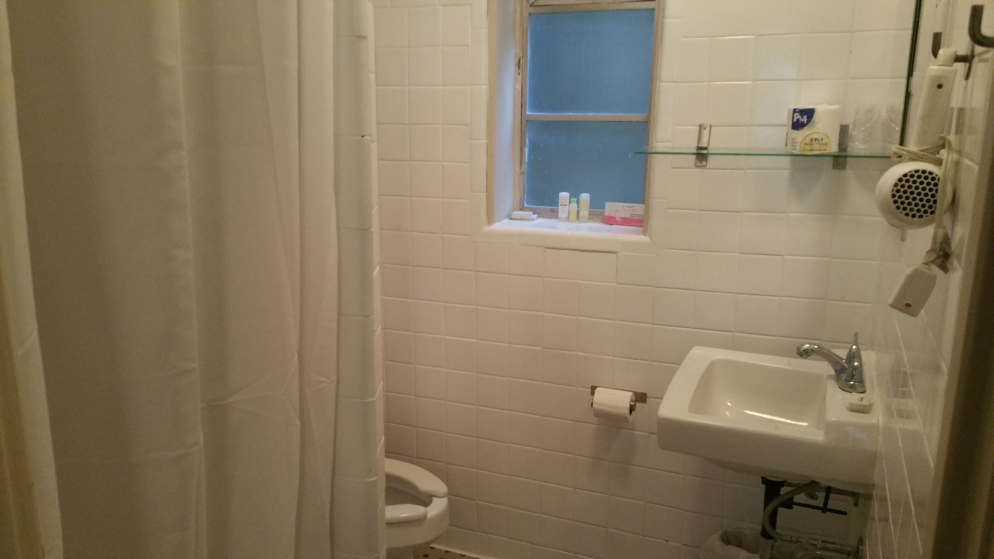 A small, white bathroom with a toilet, sink, and window.
