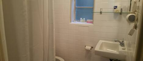 A small, white bathroom with a toilet, sink, and window.