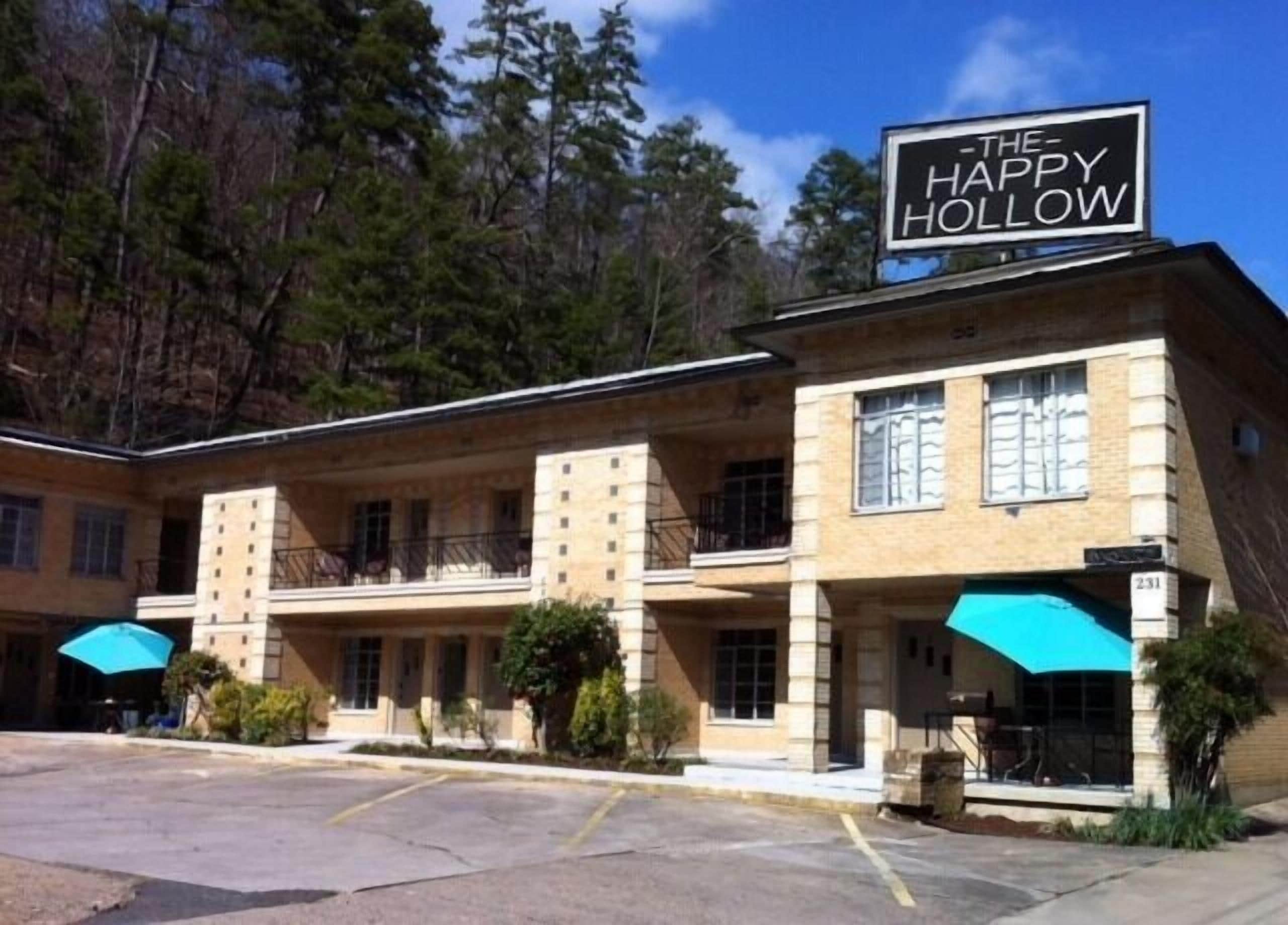 Il s’agit d’un immeuble sur lequel on peut lire l’inscription « The Happy Hollow ». Il comporte plusieurs étages, des balcons et un parking situé à l’avant.