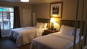 A hotel room with two beds, a window with a view of the outside, a painting on the wall, and a bedside table with a lamp. - The Happy Hollow (Hot Springs)
