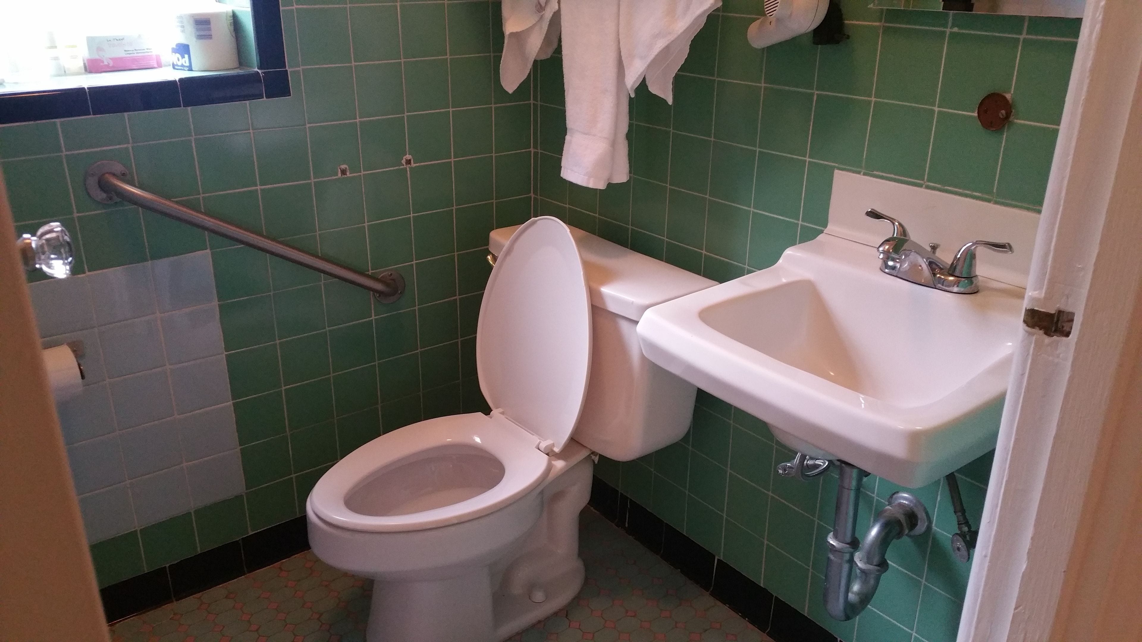 A bathroom with a white toilet, green tiled walls, a sink, and a handrail.