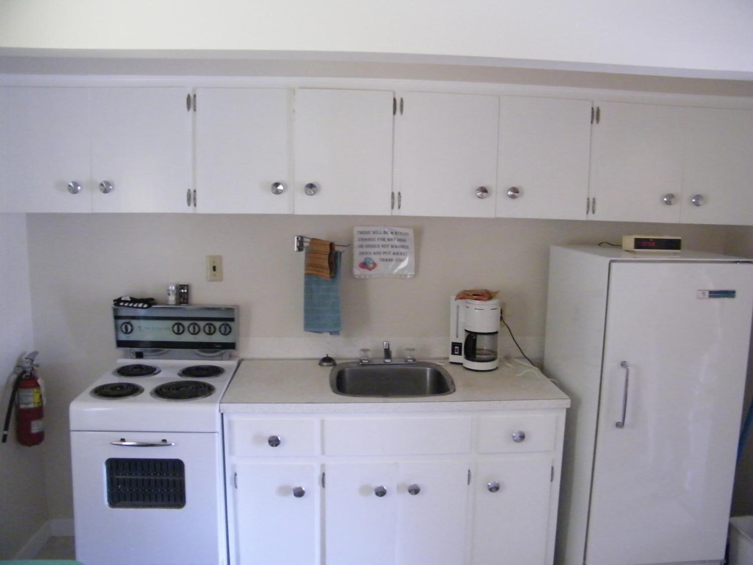 Una cocina compacta con armarios blancos, estufa, lavamanos y refrigerador.