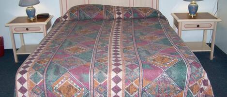 A bed with a patterned bedspread, two bedside tables with lamps, and a nightstand with a lamp.