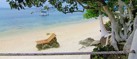 Una playa arenosa con un banco de madera, agua azul cristalina y un barco a lo lejos.