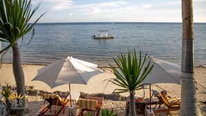 A beach with umbrellas, lounge chairs, and a boat in the water. - J&R Residence (Anda)