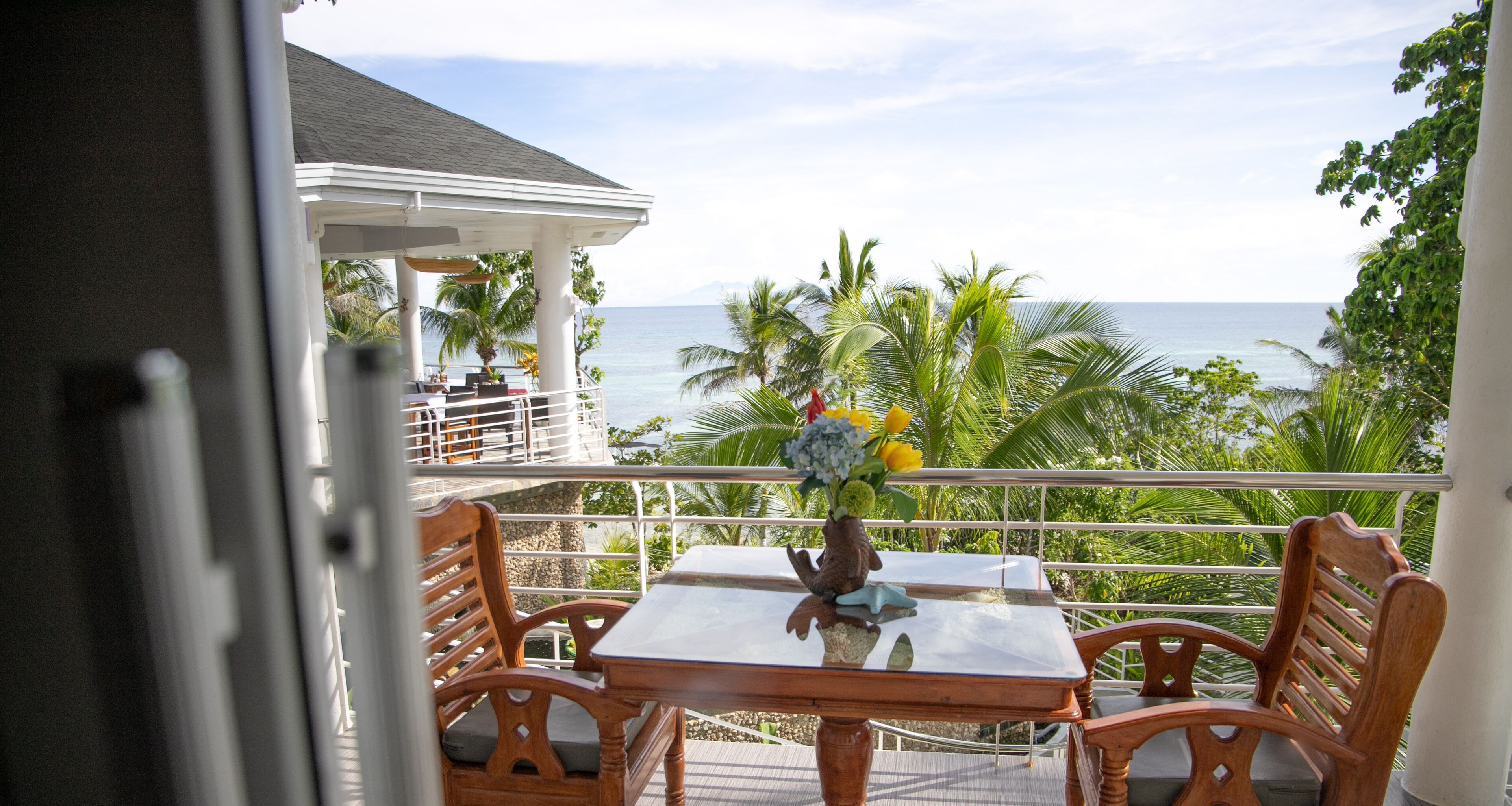 A balcony with a table and chairs, overlooking a beach and ocean.