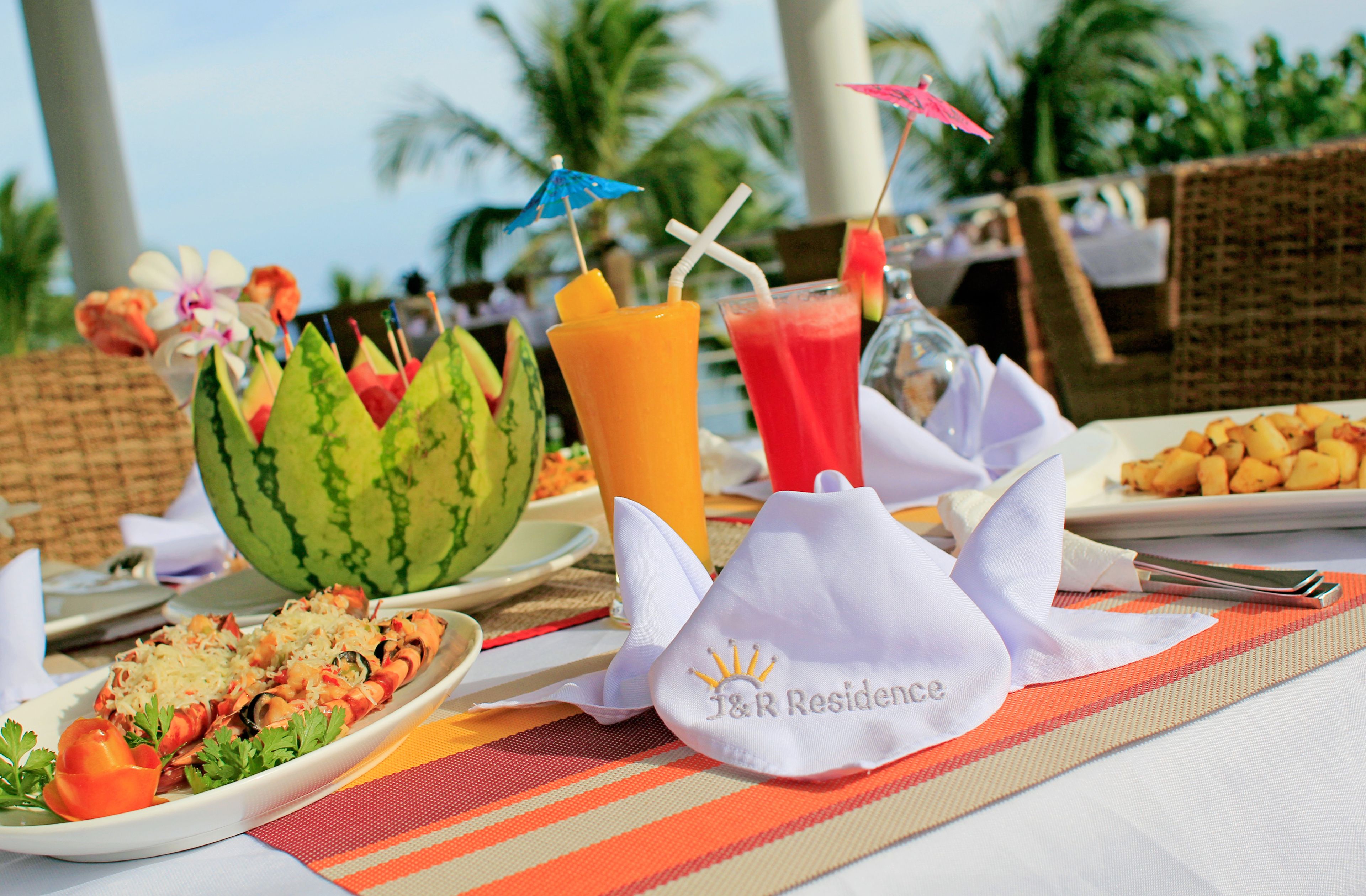 A table set with a watermelon, a plate of food, and drinks with straws and umbrellas.