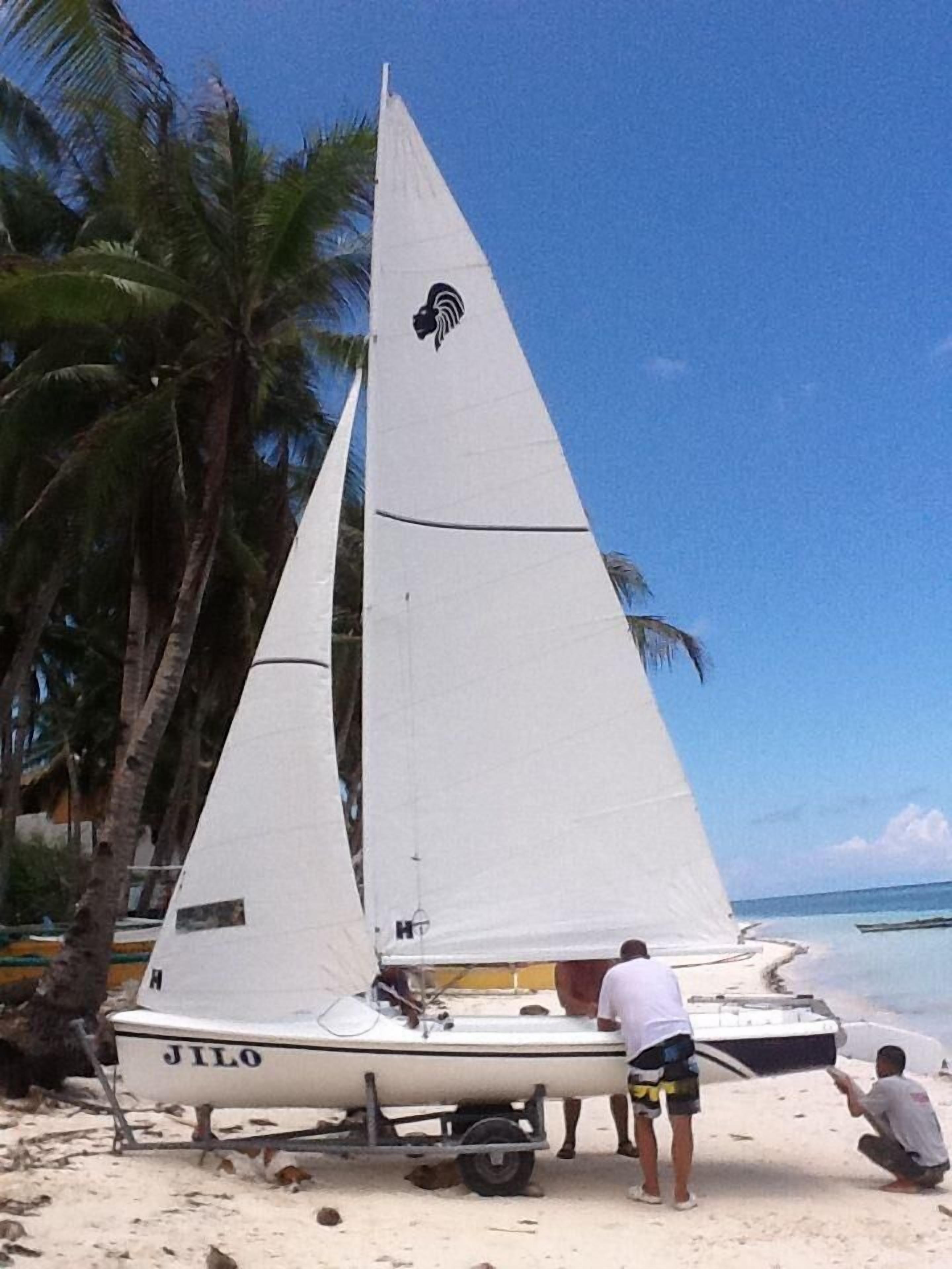 A sailboat named 'JILO' on a sandy beach with palm trees and the ocean in the background.