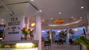 Un restaurante con vistas al mar, que cuenta con una zona de bar, mesas al aire libre y un letrero que dice "SEA BREEZE BAR & RESTAURANT".