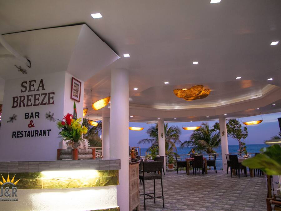 Un restaurante con vistas al mar, que cuenta con una zona de bar, mesas al aire libre y un letrero que dice "SEA BREEZE BAR & RESTAURANT".