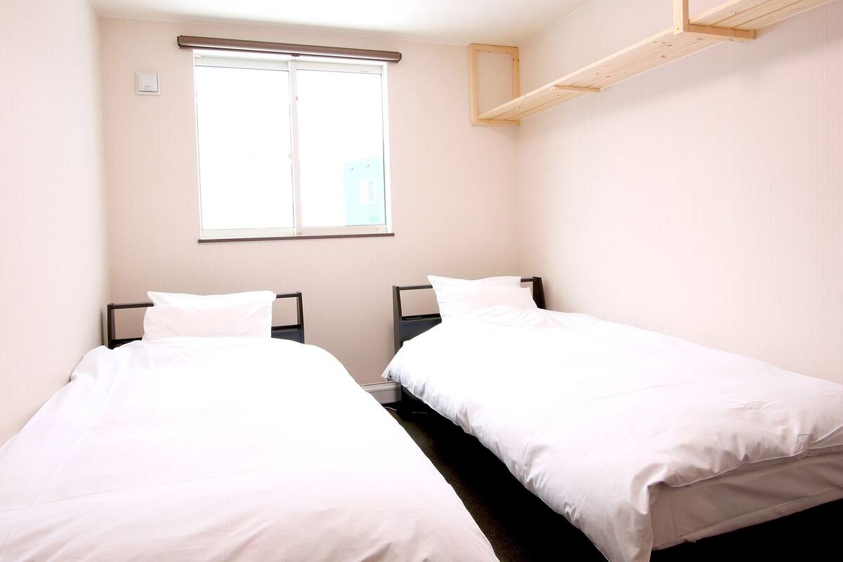 A room with two single beds, a window, and a wooden shelf.