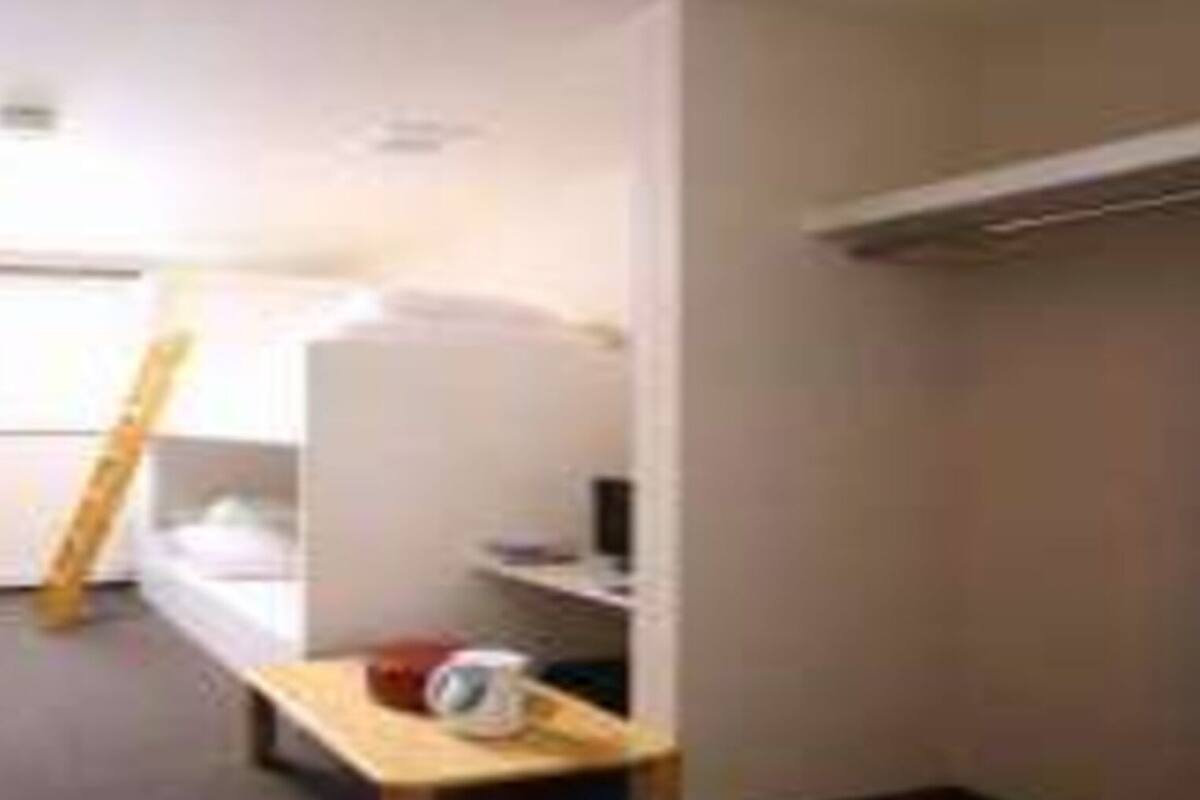 A compact hotel room with a bunk bed, a small desk with a chair, and a window providing natural light.