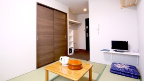 Una habitación con puerta corredera, una mesita con hervidor, televisor en estante y cama tipo futón.