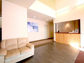 A reception area with a wooden counter, a beige sofa, and a framed picture on the wall. - Lodge Koropokkuru (Kutchan)