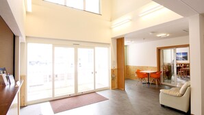Un hallo espacioso con mostrador de recepción, una zona de estar con sillas naranjas, un sofá blanco y vistas a través de amplias puertas de cristal.