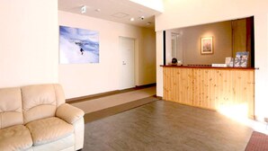 Un área de recepción con un mostrador de madera, un sofá color crema y un cuadro en la pared.