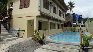 Un edificio de dos pisos con piscina, escalera exterior y macetas.