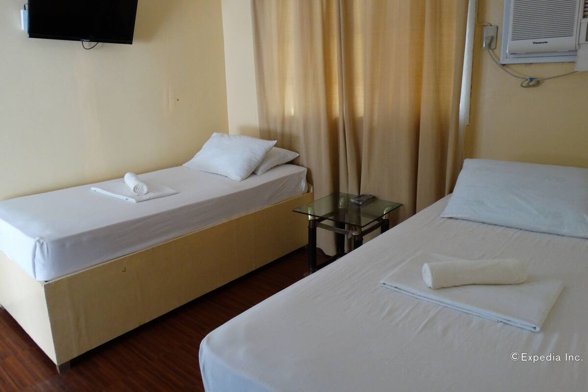 Habitació d'hotel amb dos llits individuals, un televisor fixat a la paret, una taula petita i una finestra amb cortines.
