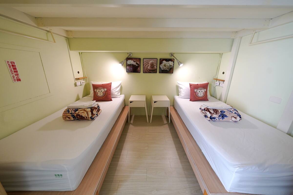 Une chambre avec deux lits simples, une petite table et des lampes fixées au mur.