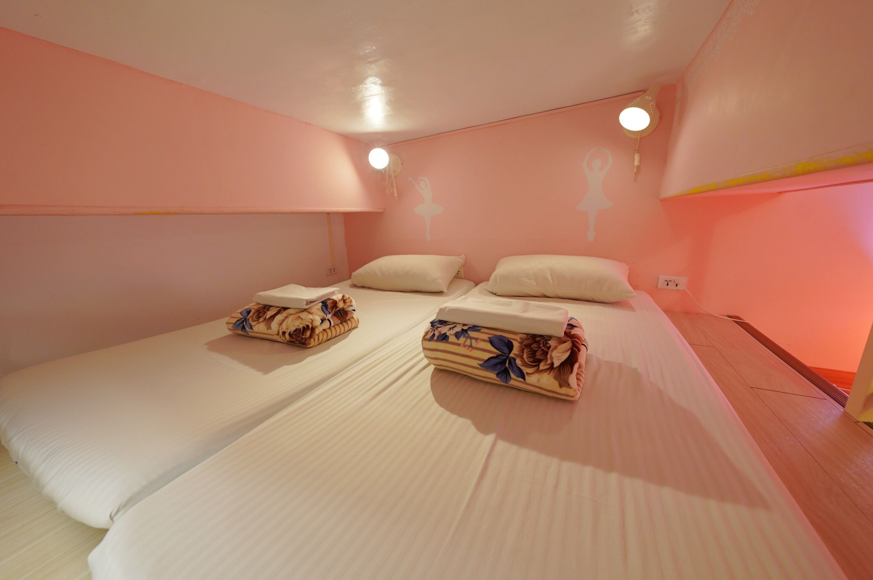 Un dormitorio con dos camas individuales, suelo de madera y pared rosa.