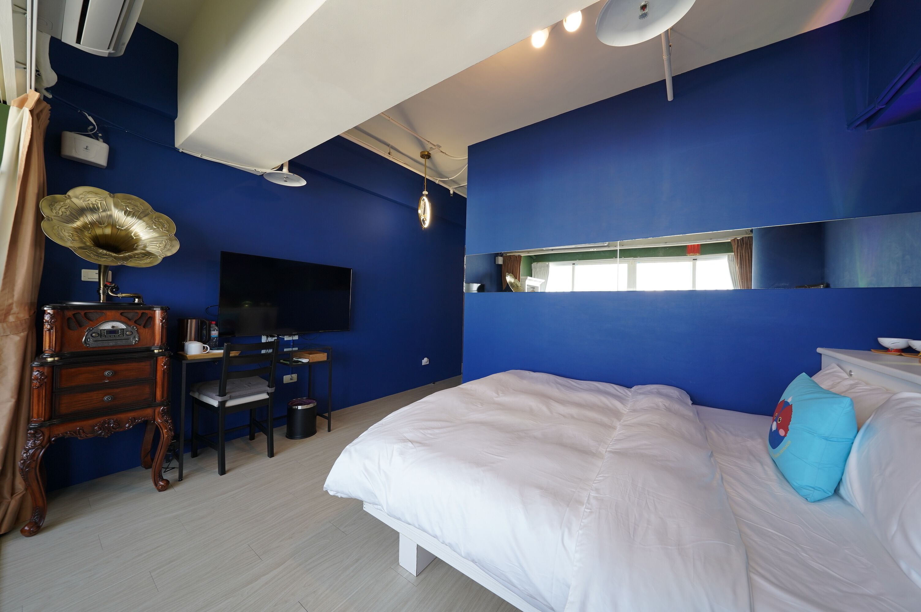 A room with a bed, a desk with a chair, a television, and a large mirror.