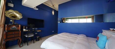A room with a bed, a desk with a chair, a television, and a large mirror.