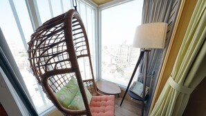 A wicker chair with a cushion, a small table, and a lamp near a window with a view of buildings. - An Lan Jie Hotel - Hostel (Chiayi City)