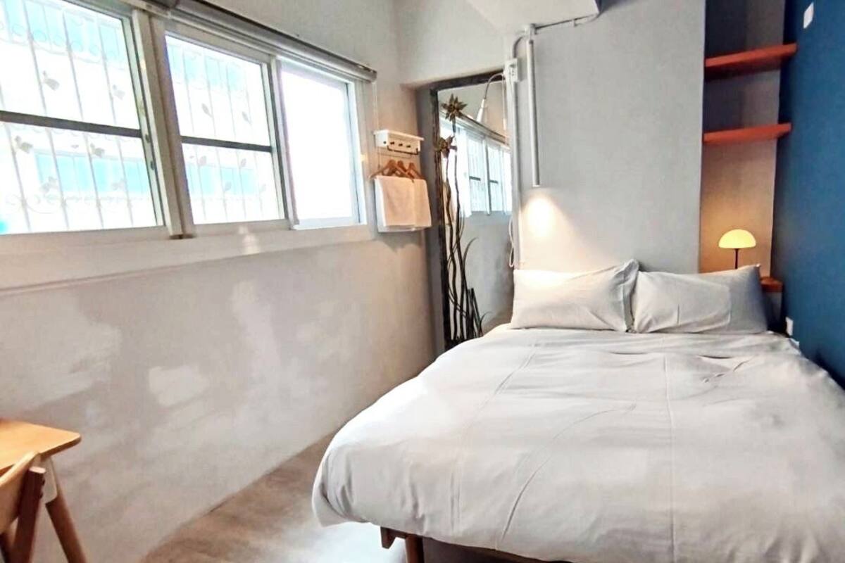 Une chambre à coucher avec un lit, une petite table, une fenêtre et une lampe.