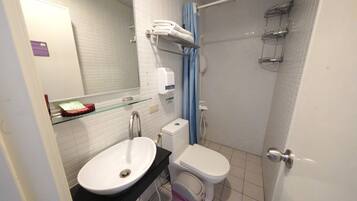 A bathroom with a white sink, toilet, and shower. There are towels on a rack and a soap dispenser on the wall.