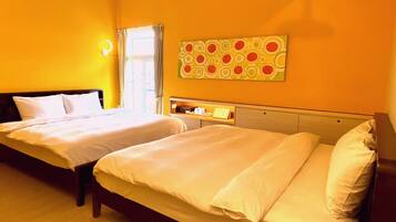 A hotel room with two beds, a window with curtains, a wall art piece, and a bedside table with a lamp.