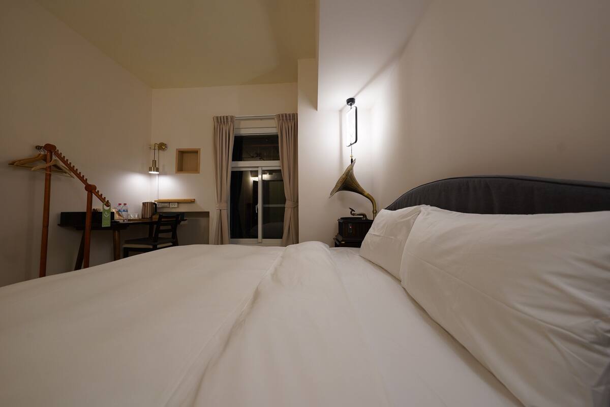 Une chambre d’hôtel comprenant un lit, un bureau avec une chaise, une armoire et une fenêtre avec des rideaux.