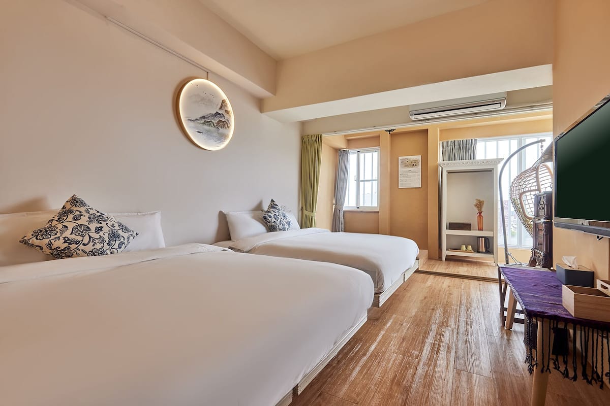 Une chambre d’hôtel avec deux lits, un bureau avec un ordinateur, un miroir et une vue sur l’extérieur.