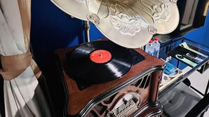 A vintage gramophone with a large horn, a record player, and a small shelf with bottles and a remote control. - An Lan Jie Hotel - Hostel (Chiayi City)
