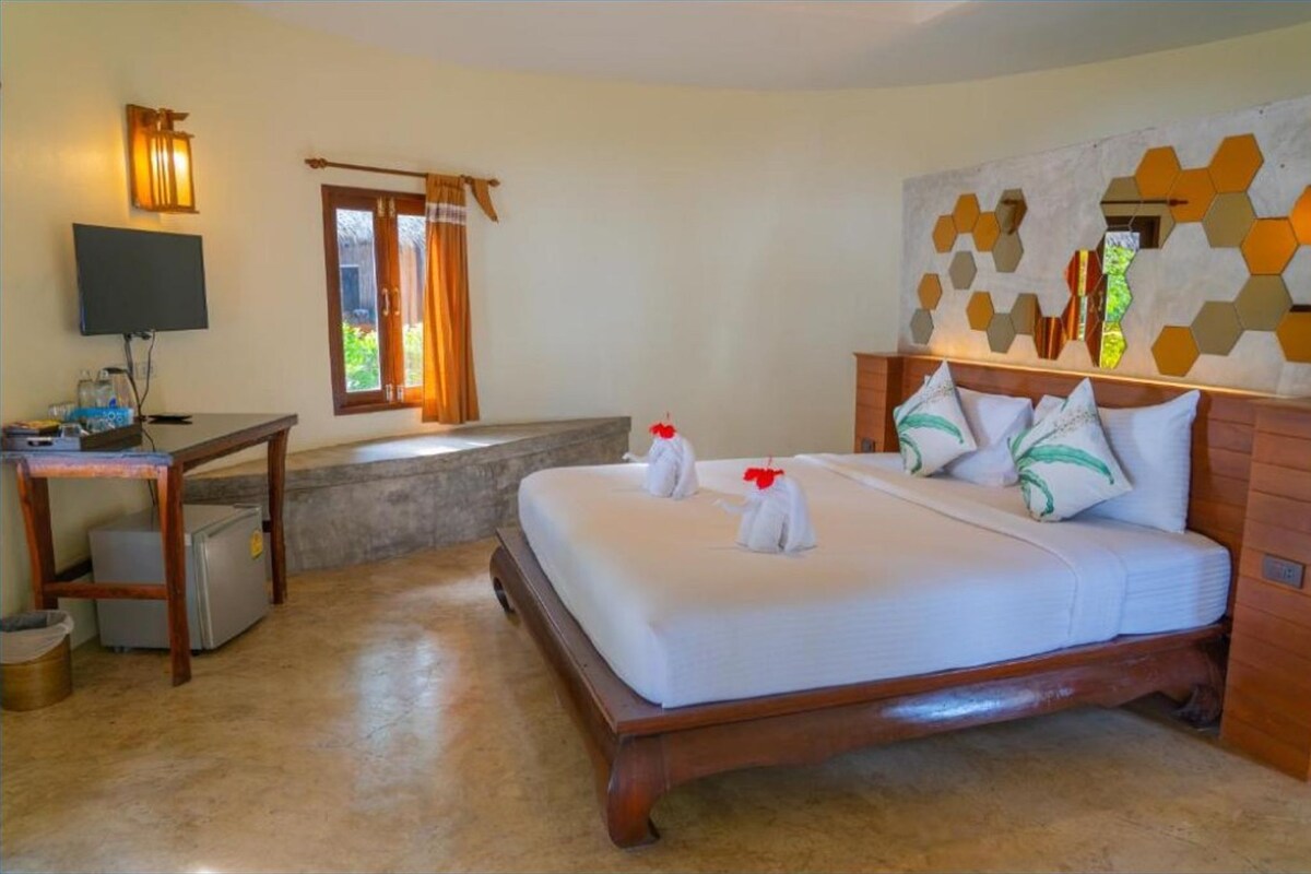 Habitación de hotel con cama, escritorio, televisor y ventana con cortinas.