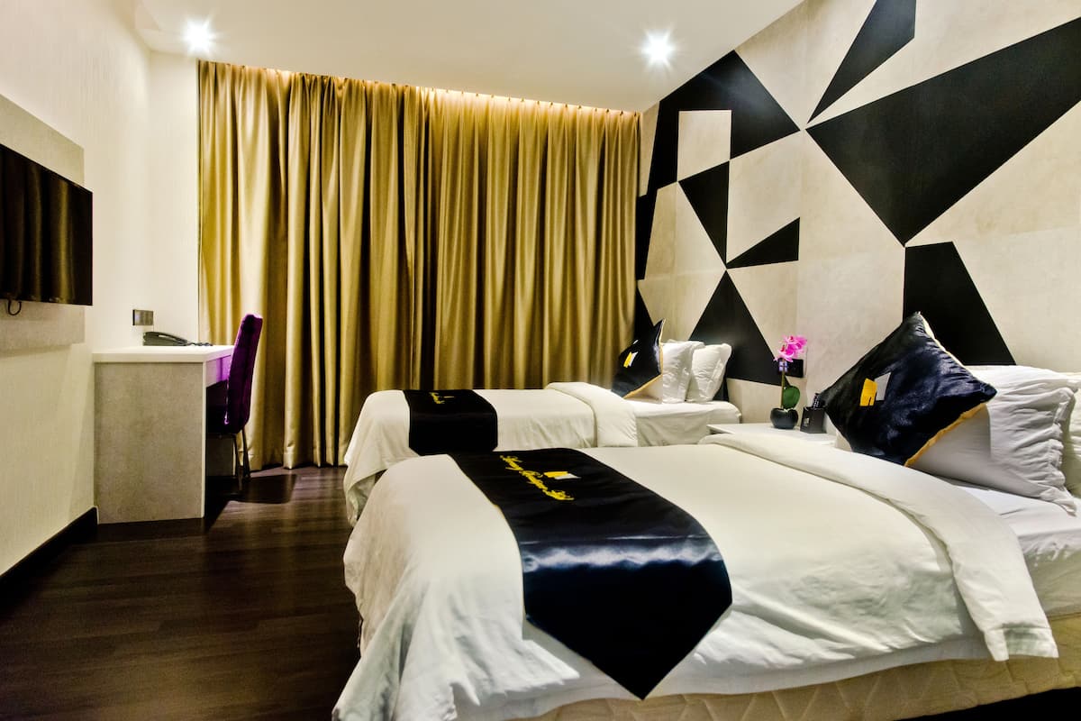 Une chambre d’hôtel avec un grand lit, un bureau et une chaise. Il y a un rideau à la fenêtre et les murs sont ornés d’un motif géométrique.