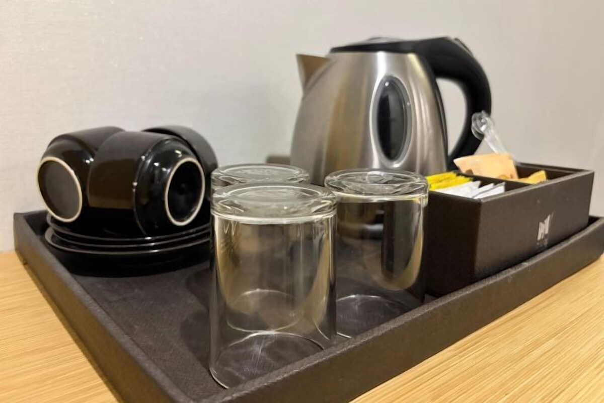 A tray with a kettle, two black cups, and three clear glasses.