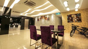 A modern hotel lobby with a reception desk, purple chairs, a glass table, and a bicycle rack. - Mercury Boutique Hotel (Malacca City)