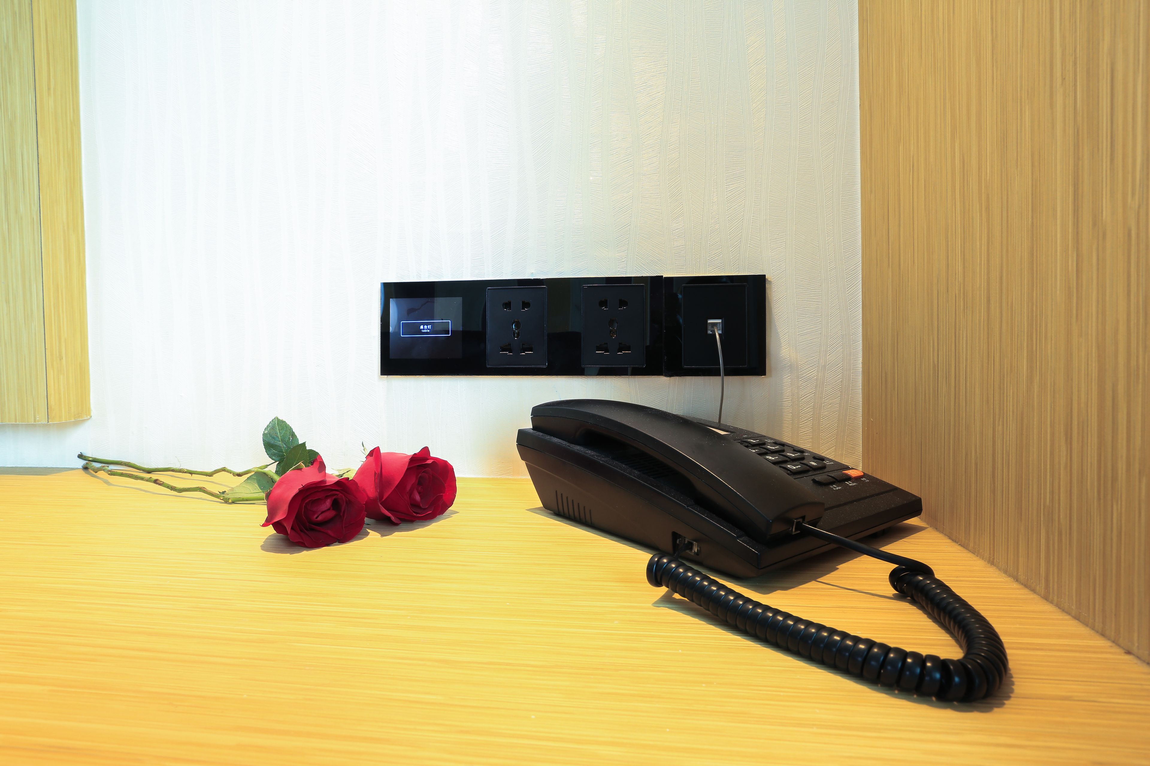 A wooden desk with a telephone, a power strip, and two red roses.