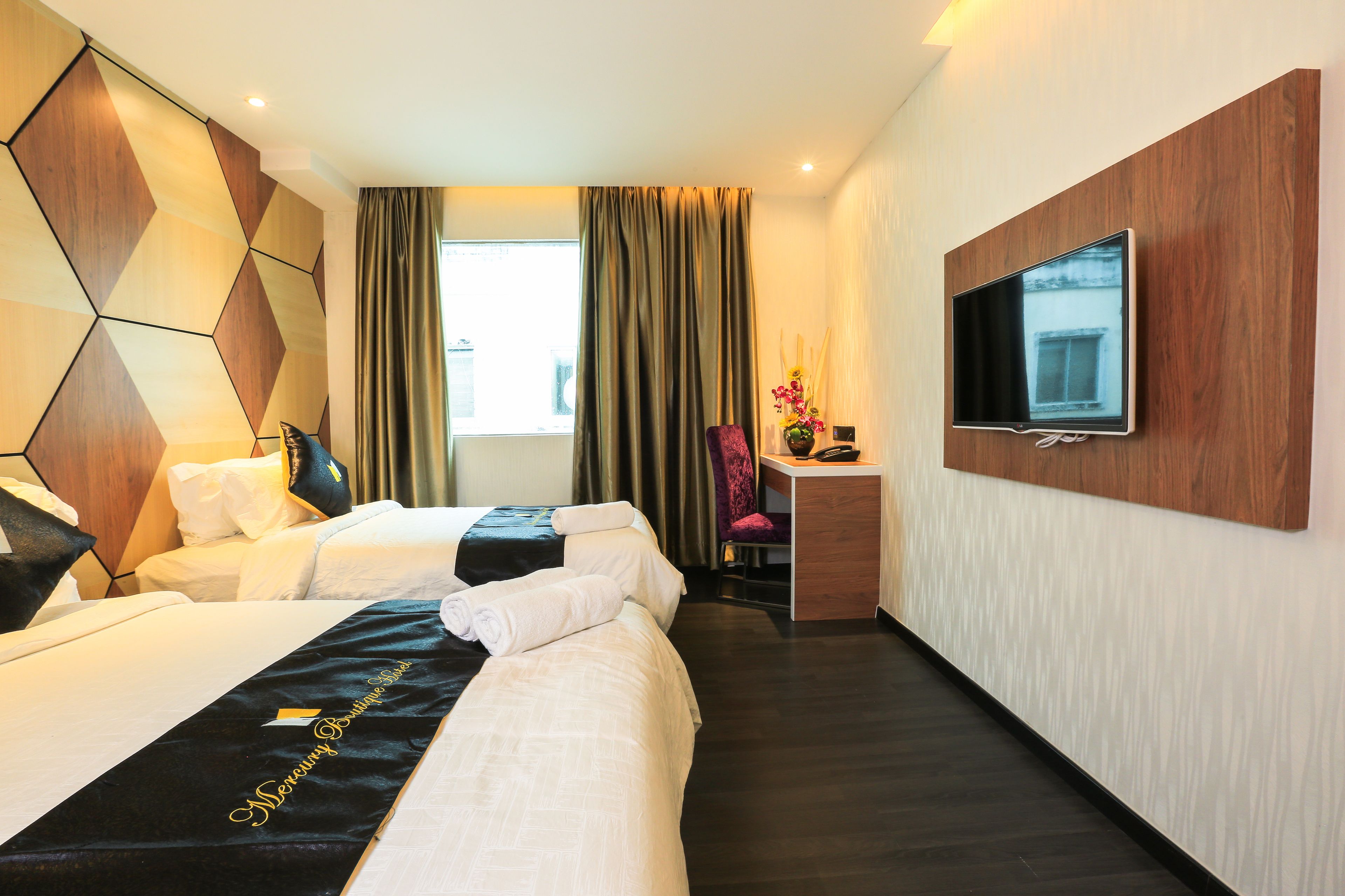 A hotel room with two beds, a desk with a chair, a television mounted on the wall, and a window with curtains.