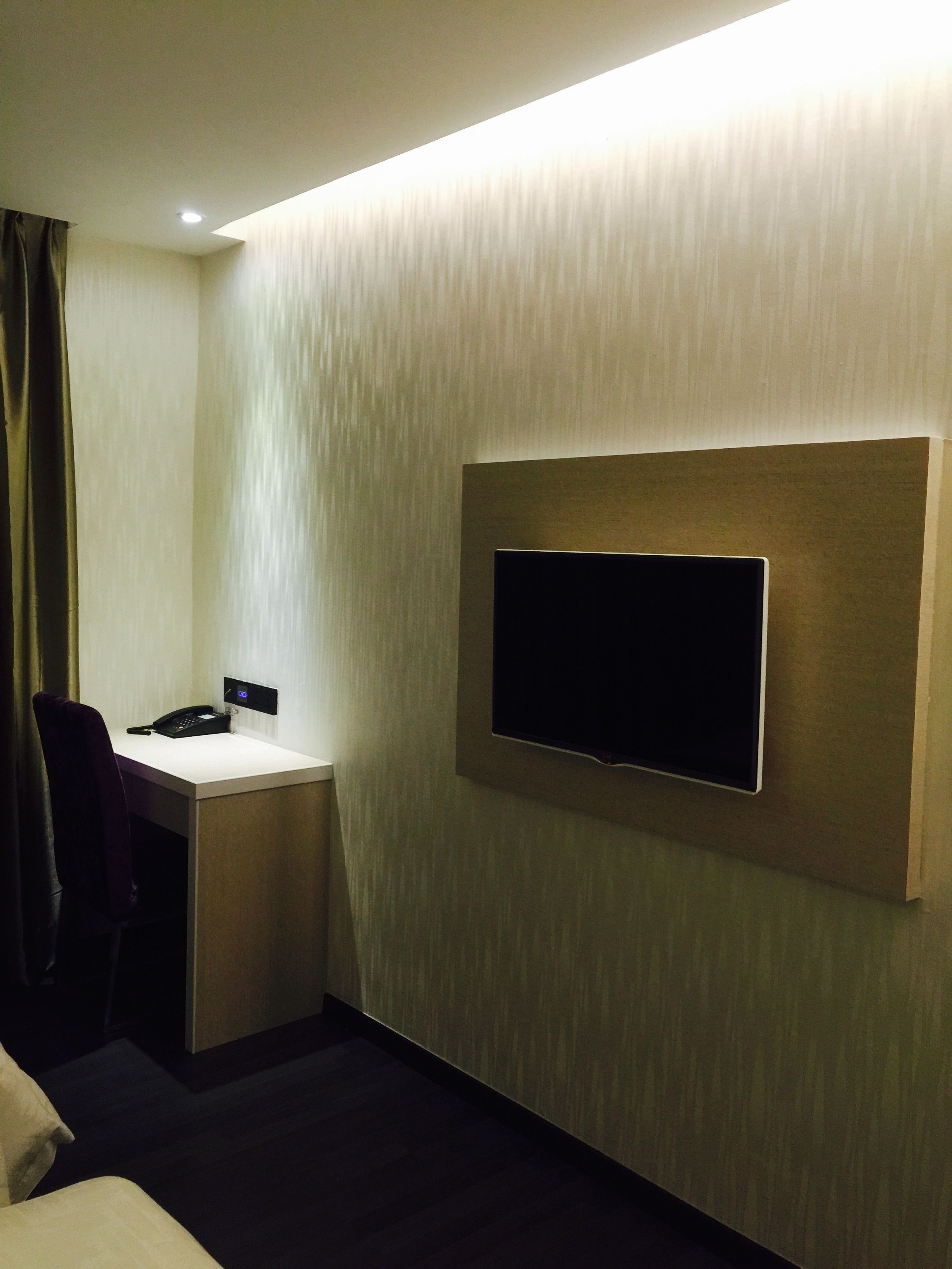 Habitación de hotel con televisor de pantalla plana en la pared, un escritorio con teléfono y una silla.