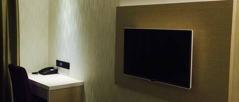 Habitación de hotel con televisor de pantalla plana en la pared, un escritorio con teléfono y una silla.