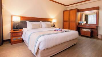 A hotel room with a large bed, wooden headboard, bedside lamps, a nightstand, a dresser, a mirror, and a small bench.
