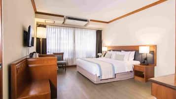 Habitación de hotel con cama, televisor, escritorio, silla y ventana con cortinas.